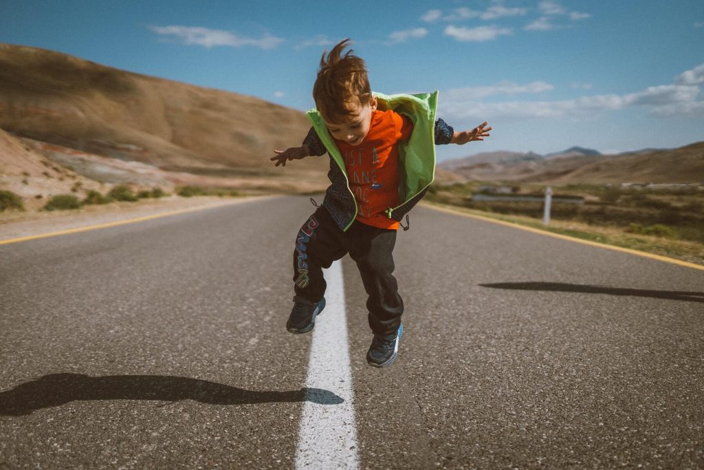Child jumping in road with mountains in background